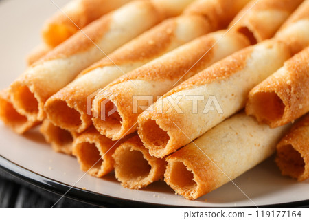 Sweet Russian cigarettes are tender tubes baked to a crispy golden crust close-up in a plate. Horizontal 119177164