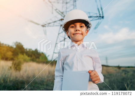 Little kid pretending engineer or manager with safety helmet, with papers documents. Electrical industry profession, serious smart child on transmission power lines background. 119178072