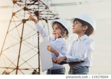 Little kids pretending engineers or managers with safety helmets, reading papers documents. Electrical industry profession, serious smart children on transmission power lines background. 119178084