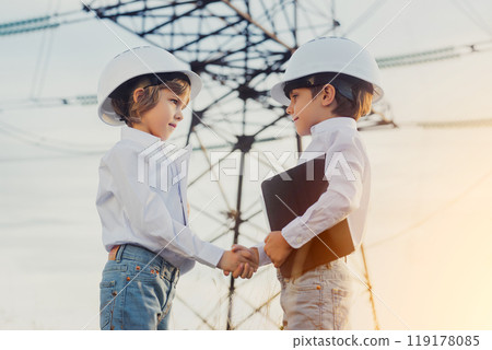 Little kids shaking hands. Handshake, welcome to team, introduction or hiring. Electrical industry job, serious smart children on Electricity Pylons background. Green energy sustainability, renewable Little kids shaking hands. Handshake, welcome to team, introduction or hiring. Electrical industry job, serious smart children on Electricity Pylons background. Green energy sustainability, renewable 119178085