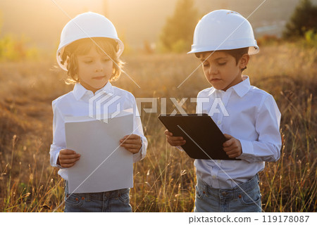 Little kids playing as engineers or managers with safety helmets, using tablet. Electrical industry profession, serious smart children on transmission power lines background. 119178087