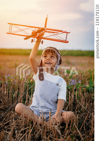 Smiling interested 5 years old child boy playing with wooden airplane, discovering future profession interest, dreamer kid flying, traveling on summer field. Creative dream, fantasy, childhood 119178110