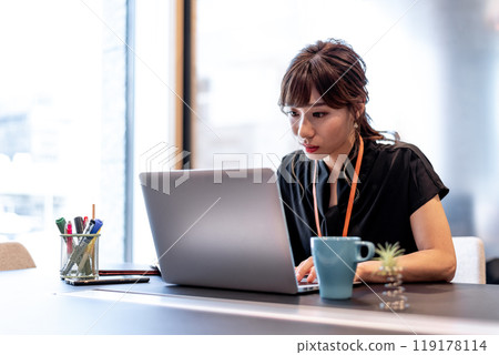 A woman working while looking closely at a computer 119178114