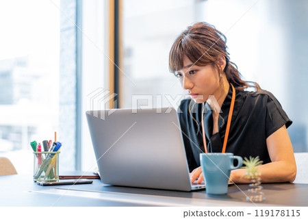 A woman working while looking closely at a computer 119178115