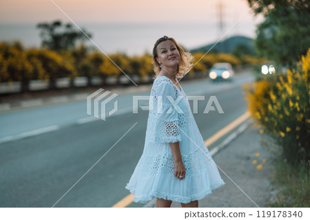 A woman in a white dress is standing on the side of a road 119178340