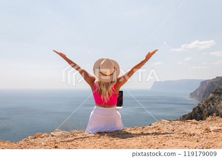 A woman is sitting on a beach with her arms outstretched, wearing a pink top A woman is sitting on a beach with her arms outstretched, wearing a pink top 119179009