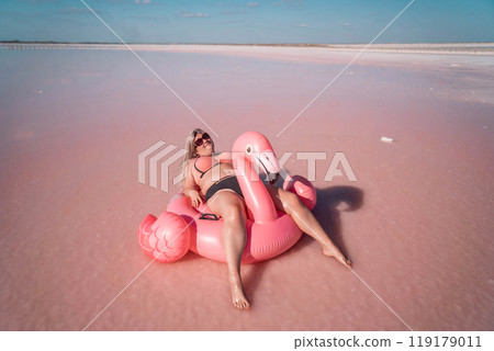 Pink Lake Flamingo Float Summer Vacation - Woman enjoys summer vacation on a pink inflatable flamingo float in a pink lake. Pink Lake Flamingo Float Summer Vacation - Woman enjoys summer vacation on a pink inflatable flamingo float in a pink lake. 119179011