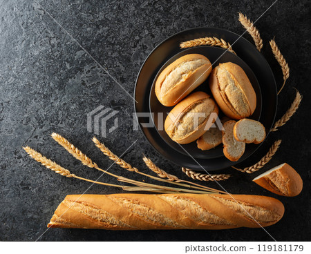 Baguette, French buns, and wheat ears on a black stone table. Baguette, French buns, and wheat ears on a black stone table. 119181179