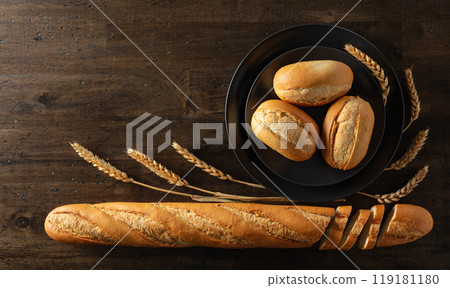 Baguette, French buns, and wheat ears on an old wooden table. Baguette, French buns, and wheat ears on an old wooden table. 119181180