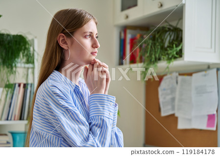Serious young woman looking out the window, in home interior 119184178