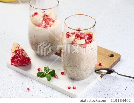 A glass of chia seeds and yogurt, with banana pieces and pomegranate seeds added to the dessert 119184402