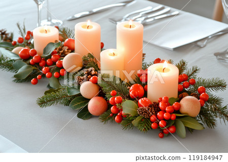 Festive Christmas centerpiece featuring three lit candles, pine cones, and ornaments on a white table. Holiday decor 119184947