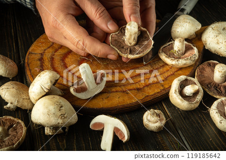Male hands holding champignon or agaricus mushroom. Sorting and cleaning mushrooms on the kitchen table before adding to food Male hands holding champignon or agaricus mushroom. Sorting and cleaning mushrooms on the kitchen table before adding to food 119185642