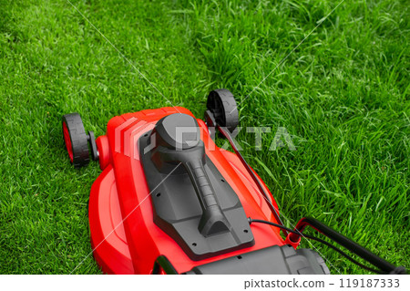 The process of mowing the lawn with a lawnmower. Red and black lawnmower on green grass web size 119187333