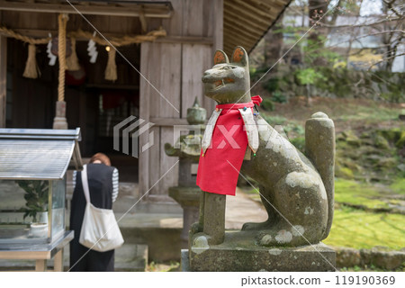 Kitsune fox statue with woman pray at Homangu Kamado shrine 119190369