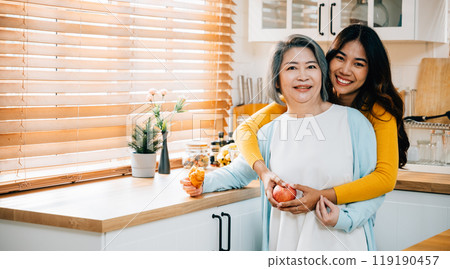 In their cozy kitchen, a grandmother and her adult daughter share a touching moment. The daughter is assisting her mother, showcasing the beauty of family bonding and care. In their cozy kitchen, a grandmother and her adult daughter share a touching moment. The daughter is assisting her mother, showcasing the beauty of family bonding and care. 119190457