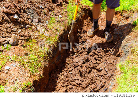 On construction site, worker digs trench with shovel for drainage pipe 119191159