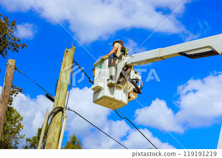 Technician repairs power line pole using hydraulic tower mounted bucket while working on electrical power system after hurricane. Technician repairs power line pole using hydraulic tower mounted bucket while working on electrical power system after hurricane. 119191219