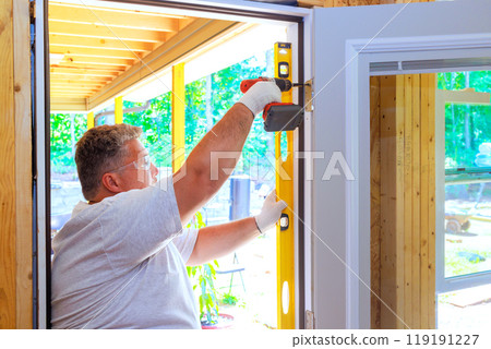 Professional carpenter worker installs front door of new house 119191227