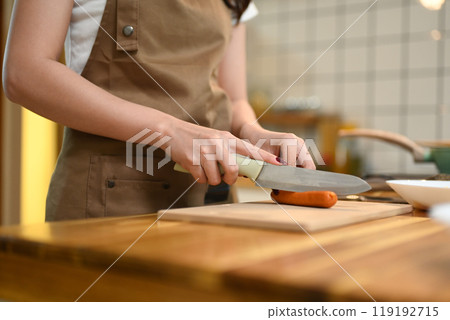 Close up of a woman cutting a sausage on wooden cutting board preparing ingredients for a meal 119192715