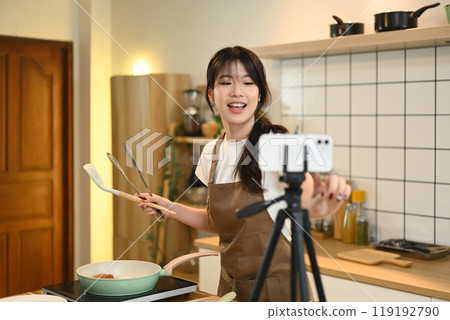 Cheerful young woman recording a cooking tutorial in a modern kitchen 119192790