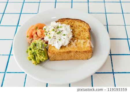 A beautifully colorful breakfast plate featuring crispy toast, ripe avocado, smoked salmon, and a rich, creamy topping 119193359