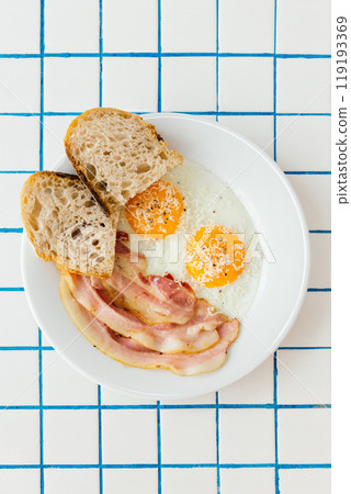 Indulge in a hearty breakfast plate that includes perfectly fried eggs, crispy bacon, and warm, toasted bread 119193369