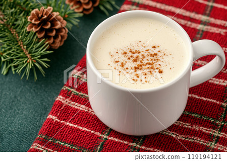 A close-up of eggnog garnished with pinecones and holly, set on a soft background, evoking festive Christmas atmosphere 119194121