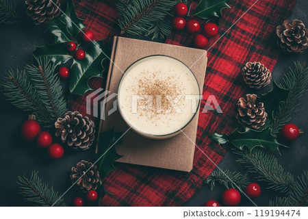 Brown recipe book next to creamy eggnog drink with spices. Pinecones and holiday greenery create festive atmosphere. 119194474