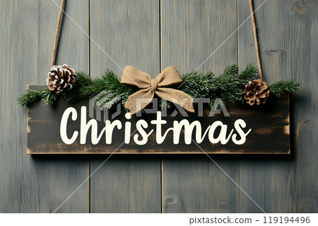 A wooden sign hangs against a blue backdrop, message Merry Christmas. Pine branches and cones add a natural touch A wooden sign hangs against a blue backdrop, message Merry Christmas. Pine branches and cones add a natural touch 119194496