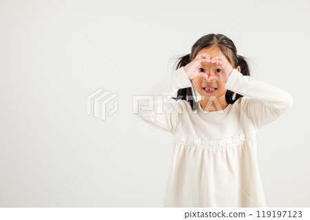 A smiling Asian young kid girl shows confidence, creating a heart shape with fingers and hands on white background. Portrait of kindergarten child sending love for Valentine's Day A smiling Asian young kid girl shows confidence, creating a heart shape with fingers and hands on white background. Portrait of kindergarten child sending love for Valentine's Day 119197123