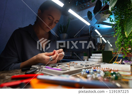 Tools for handicrafts, craftsman at his workplace in the workshop. Wide angle view of the craftsman who assembles bracelets from stones Tools for handicrafts, craftsman at his workplace in the workshop. Wide angle view of the craftsman who assembles bracelets from stones 119197225