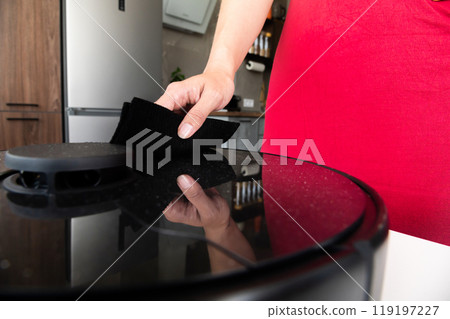 Young Caucasian woman dusting her home robot smart vacuum cleaner. Home appliance maintenance 119197227
