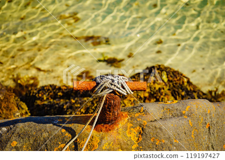 Old rusty mooring bollard with rope. Old rusty mooring bollard with rope. 119197427
