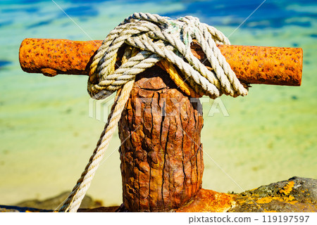 Old rusty mooring bollard with rope. 119197597