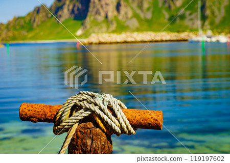 Old rusty mooring bollard with rope. 119197602