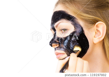 Woman applying black mud mask to face 119197802