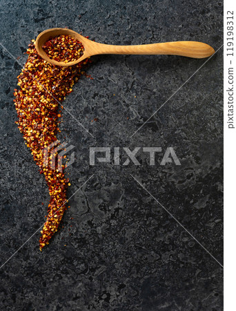 Flakes of red chili pepper in wooden spoon on a black stone background. Flakes of red chili pepper in wooden spoon on a black stone background. 119198312