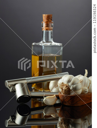 Garlic bulbs, garlic press, and bottle of vegetable oil. 119198324
