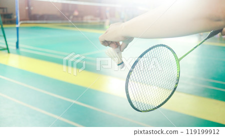 The badminton player holding a white shuttlecock and racket and standing at the net ready to serve. The badminton player holding a white shuttlecock and racket and standing at the net ready to serve. 119199912