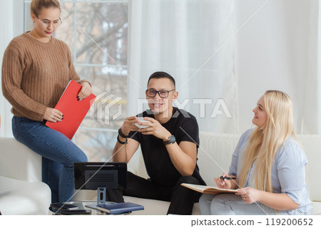 Three people are sitting on a couch, one of them holding a red folder 119200652