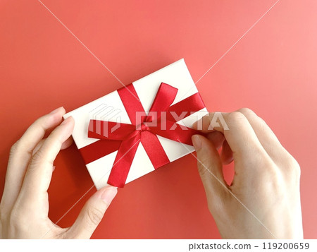 A woman's hand untying the red ribbon of a gift box 119200659
