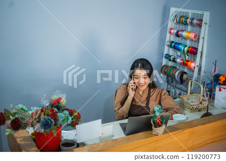 Asian girl employee making a phone call while working behind the counter 119200773