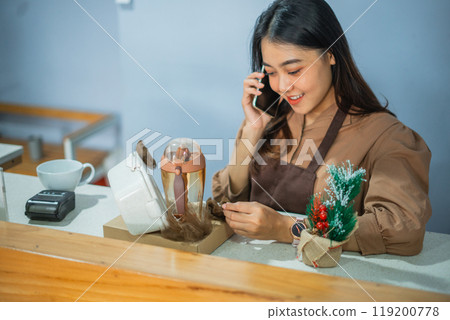 female shop assistant is on the phone telling her about a gift order 119200778