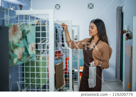 shopkeeper in an apron arranges items on a display shelf 119200779