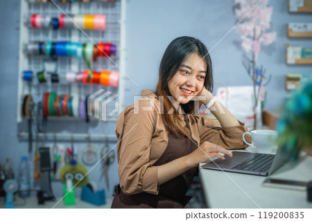 beautiful shop owner using a laptop behind the counter of a souvenir shop 119200835