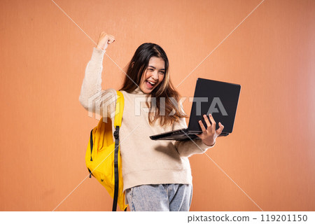 An excited student celebrates success with a laptop and backpack, feeling joyful 119201150