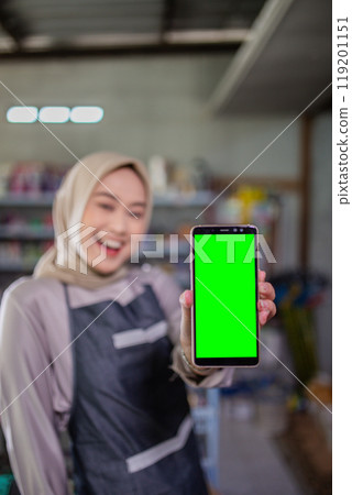 Happy Woman Holding Smartphone with Green Screen in a Creative Workspace 119201151