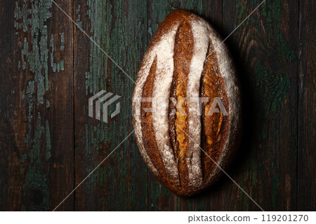 Baked rye homemade bread with malt, oval shape, sprinkled with flour on a wooden background. 119201270