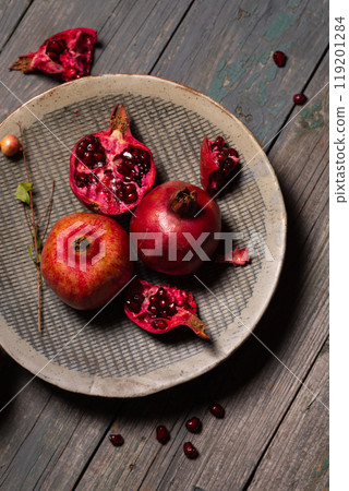 Juicy pomegranates whole and open in a ceramic gray plate on a gray wooden background Juicy pomegranates whole and open in a ceramic gray plate on a gray wooden background 119201284